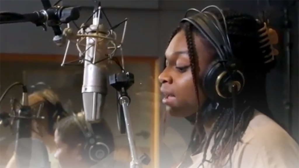 Photo d'une élève qui chante dans un micro dans un studio d'enregistrement.